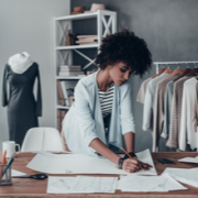 Micro-entrepreneur travaillant sur des croquis dans son atelier de travail près de vêtements accrochés aux racks
